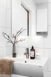 a Nordic bathroom with white tiles, a white sink, a large mirror and a branch arrangement