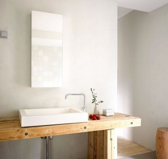 a light-colored wooden vanity, a rectangular mirror, a stool and a shower space with a wooden floor