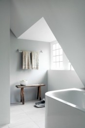 a small attic Nordic bathroom with a small tub, a bench, printed towels and much natural light