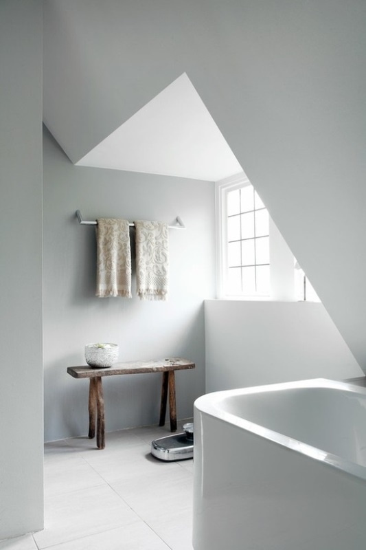 a small attic Nordic bathroom with a small tub, a bench, printed towels and much natural light