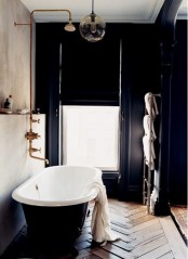 an navy art deco bathroom with a vintage tub, brass faucets and Roman shades