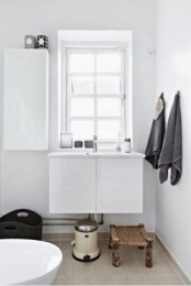 a small white Nordic bathroom with a wicker stool, a tub, a vanity and a closed storage unit