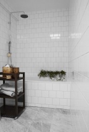 a small bathroom with white and grey marble tiles, adark stained storage unit and some potted plants