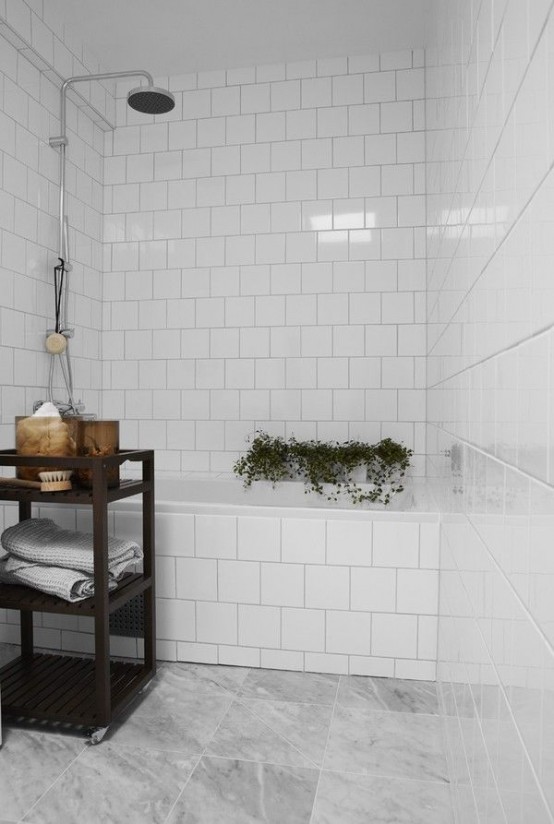 a small bathroom with white and grey marble tiles, adark stained storage unit and some potted plants