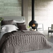 a neutral rustic bedroom with wood clad walls, elegant furniture, a suspended hearth and cozy knit bedding