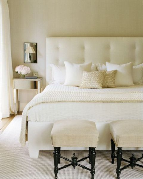 a creamy modern bedroom with a large and comfy bed, upholstered stools and mirror nightstands and mirrors over them