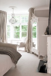 a neutral vintage bedroom done in white and greys, refined furniture, a crystal chandelier, grey linens