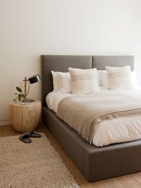 a contemporary neutral bedroom with a grey upholstered bed, neutral bedding and rugs, a wooden nightstand for a chic look