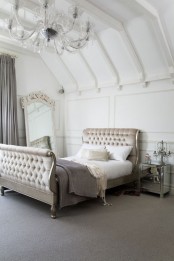 a refined neutral attic bedroom with sophisticated furniture, a crystal chandelier and an oversized mirror in a chic frame