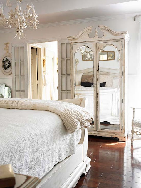 a neutral vintage bedroom with refined furniture, a mirror wardrobe, a white chandelier, layered bedding and pretty artworks