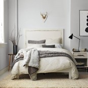 a neutral bedroom with a creamy bed, neutral bedding, branches in a vase, artworks and black touches for drama