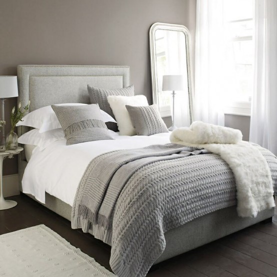 a simple neutral bedroom with taupe walls, neutral furniture, layered bedding, a mirror and lamps plus a neutral rug