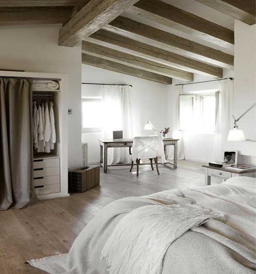 a neutral vintage bedroom with wooden beams, refined wooden furniture, a built-in wardrobe, neutral linens and table lamps