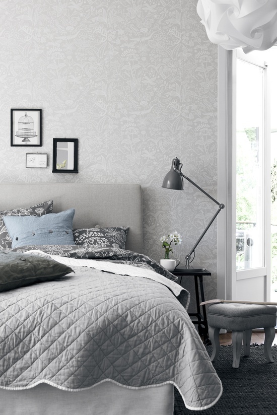 a neutral bedroom done in greys, with a printed wallpaper wall, a grey bed, grey and blue bedding and a textural pendant lamp