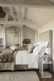 a neutral bedroom with whitewashed beams, a tan bed, layered bedding, a crystal chandelier and lamps by the bed