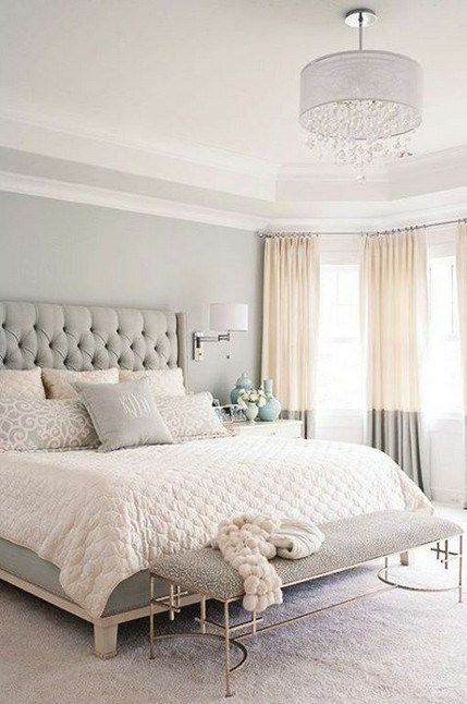 a neutral bedroom with grey walls, a chic bed with a tufted headboard and color block curtains and a crystal chandelier