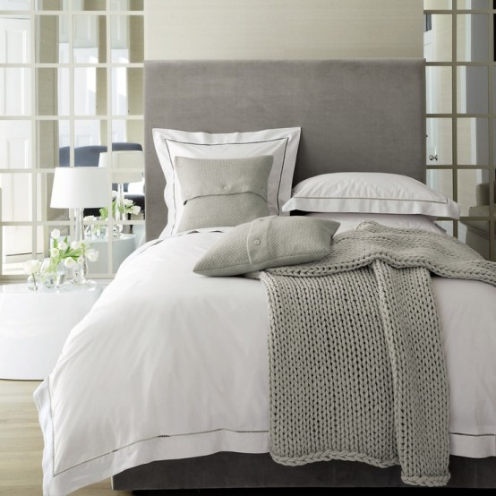 a modern bedroom with mirror panels, a grey bed, layered bedding and knit and crochet items is very light-filled