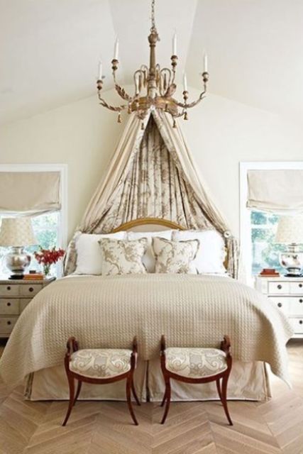 a neutral refined bedroom with a neutral bed, a floral canopy, a refined chandelier, exquisite stools