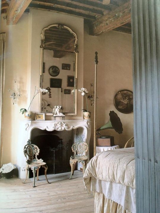 a refined Provence bedroom with plaster walls, an antique fireplace, a large mirror, a bed with a canopy, chic carved chairs and vintage decor
