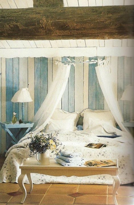 a Provence bedroom with blue and white planked walls, a bed with neutral bedding, a sheer canopy, blue vintage nightstands and a chic bench for storage at the foot of the bed