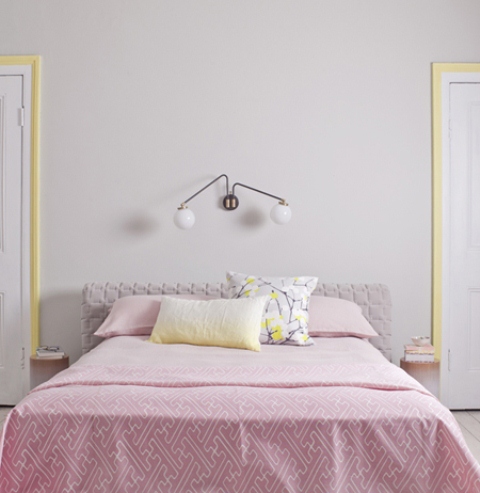 a modern feminine bedroom with grey walls, a grey upholstered bed, pink and yellow bedding and yellow frames around the doors