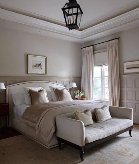 a chic neutral bedroom with paneled walls, elegant furniture, some artworks and a statement lantern over the space, shiny bedding and pillows