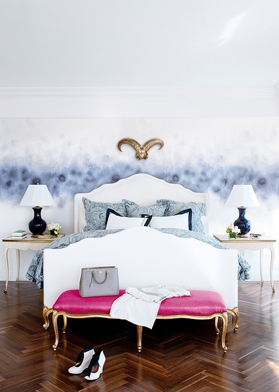 a contemporary feminine bedroom with a catchy accent wall, refined furniture, touches of gold, a pink bench and printed blue bedding