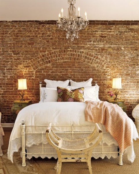 a refined girlish bedroom with an exposed brick wall, elegant white furniture, white and floral bedding and a beautiful crystal chandelier