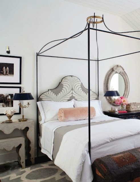 a refined and chic bedroom with a black forged canopy bed, elegant nightstands, a large dark chest and artworks plus an oval mirror is amazingly stylish