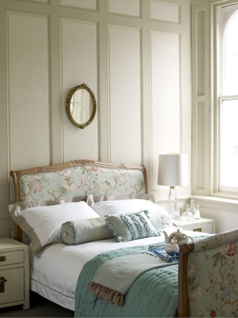 a romantic vintage bedroom done in neutrals, with paneled walls, a floral bed, neutral furniture, powder blue and neutral bedding and ruffled pillows