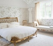 a neutral feminine bedroom with floral wallpaper walls, exquisite furniture with gold touches and a crystal chandelier