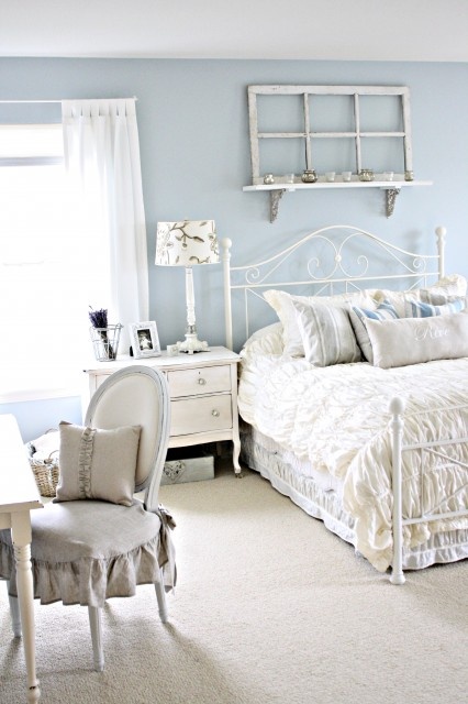 a shabby chic feminine bedroom with powder blue walls, vintage furniture in white, neutral and printed linens and a ruffled chair