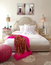 a bold feminine bedroom with a grey upholstered bed, mirrored nightstands, bold fuchsia touches and pretty artworks over the bed