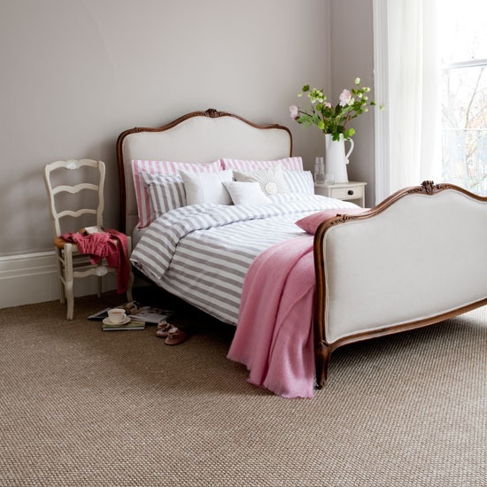 a laconic and romantic feminine bedroom with a refined white bed, striped and pink bedding, a chic chair and some pink blooms and greenery is lovely