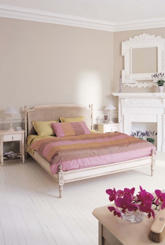 a vintage-inspired feminine bedroom with grey walls, a carved wooden bed, a faux fireplace, picture frames and blooms