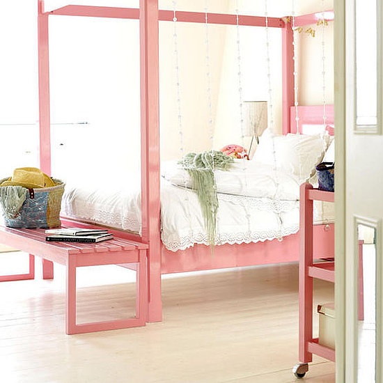 an airy feminine bedroom with a pink canopy bed and a bench, a pink console table and crystals plus simple bedding