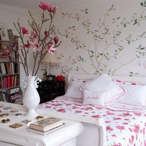 an ethereal feminine bedroom with a painted floral wall, simple yet catchy furniture, bright floral bedding and bold pink blooms on branches