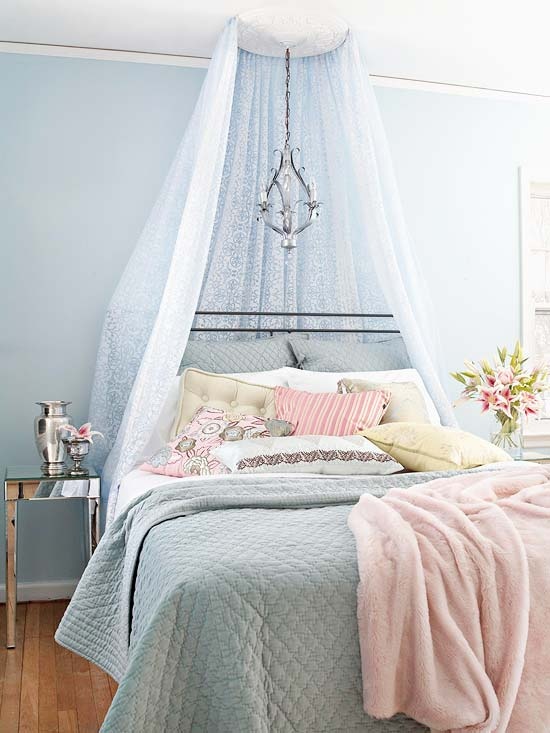 a pastel feminine bedroom with blue walls, a forged bed and a cnaopy plus a lamp, pastel blue and pink bedding