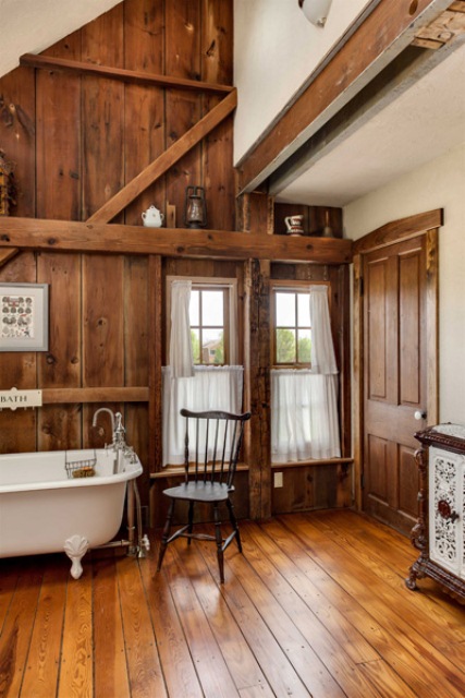 a cozy barn bathroom clad with stained wood all over, with wooden beams and a vintage bathtub on clawfoot legs