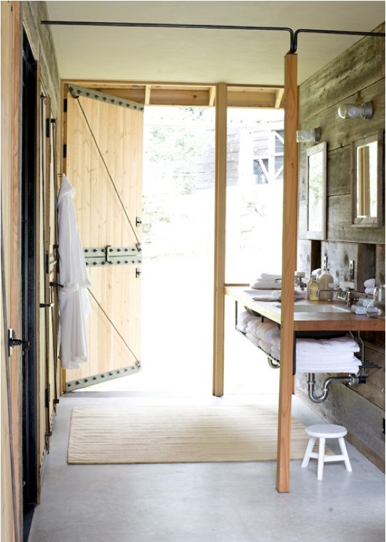 a barn bathroom clad with wood, with a floating vanity and a large door to outdoors to make the space more outdoorsy