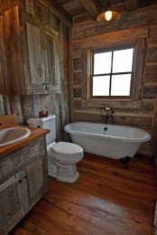 a barn bathroom fully clad with reclaimed wood, with a wall-mounted cabinet, a clawfoot tub, a neutral sink and a window