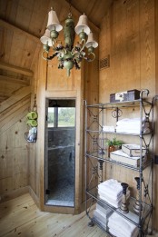 a barn bathroom clad with wood, with a shower clad with tiles, metal shelves and a refined chandelier