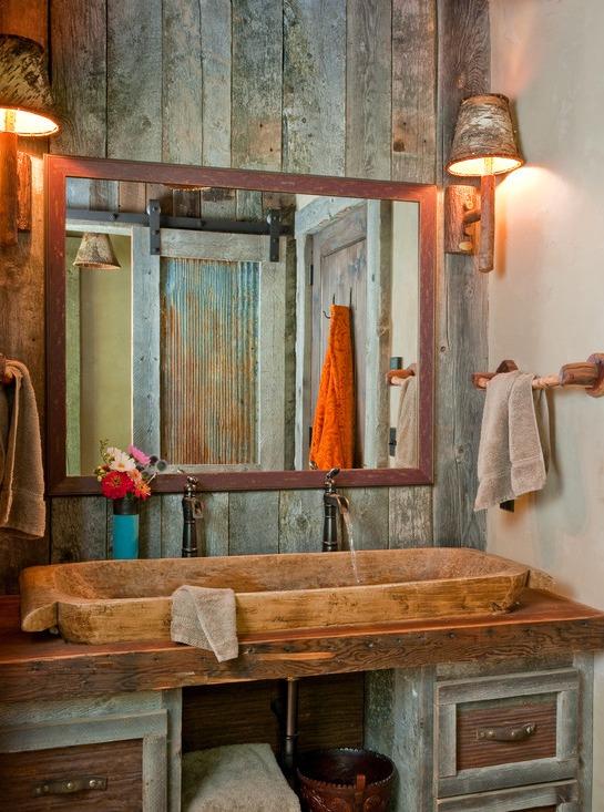 a barn bathroom clad with reclaimed wood, with a large mirror in a frame, a large vanity and a stone sink on it