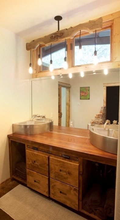 a rustic wooden vanity, a catchy chandelier with bulbs, metal sinks for a cool and cozy barn bathroom