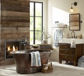 a rustic barn bathroom with a reclaimed wooden wall, wooden furniture, a built-in fireplace and a vintage metal bathtub