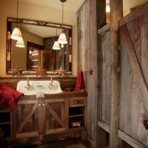 a rustic bathroom clad with reclaimed wood, with a vintage mirror, a reclaimed wooden vanity and bright towels