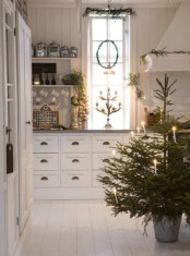 a non-decorated Christmas tree with candles in a bucket, evergreens all around the space for a cozy and natural feel