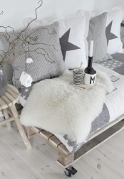 a neutral Nordic bench with grey and white Scandi pillows and white faux fur, branches and a toy house ornament for a cozy feel