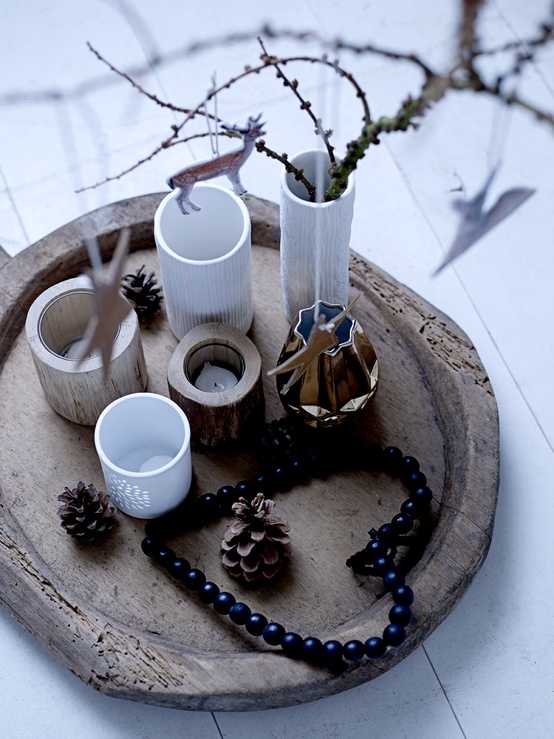 a wooden tray with wooden and neutral candleholders and a vase with branches, pinecones and beads