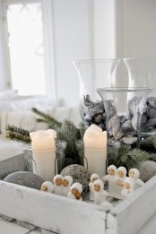 a Nordic Christmas centerpiece of a white tray, mini figurines, evergreens and pebbles plus seashells in glasses